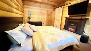 Ein Schlafzimmer einer Holzhütte mit Bett, Kissen, einem Schminktisch, einem Fernseher und einem Kamin.