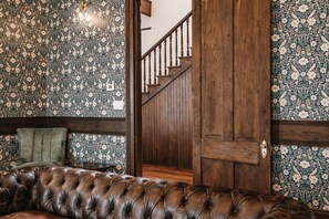 A room with a patterned wallpaper, a wooden staircase, and a leather sofa. - 9 Bedroom Historic Home With Pool and Modern Upgrades (Galveston)