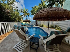 Une piscine avec des chaises longues et un parasol en chaume.