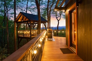 A wooden deck with a covered seating area and a grill, surrounded by trees. - Outdoor Movies w Hot Tub Fire Pit Mtn Views (Penrose)