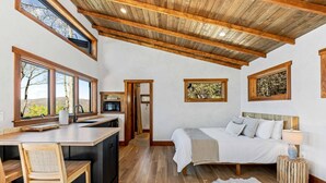 Un dormitorio con cama, mesita de noche y vistas a árboles a través de grandes ventanales.