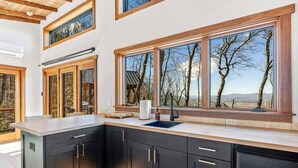 Cocina moderna con armarios oscuros, una isla grande y ventanas amplias con vistas a árboles y montañas.