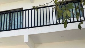 A two-story building with a white exterior, a balcony with black railings, a white door, and a window with a decorative frame.