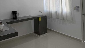 A room with a ceiling fan, a coffee machine, a small refrigerator, a window with curtains, and a door.