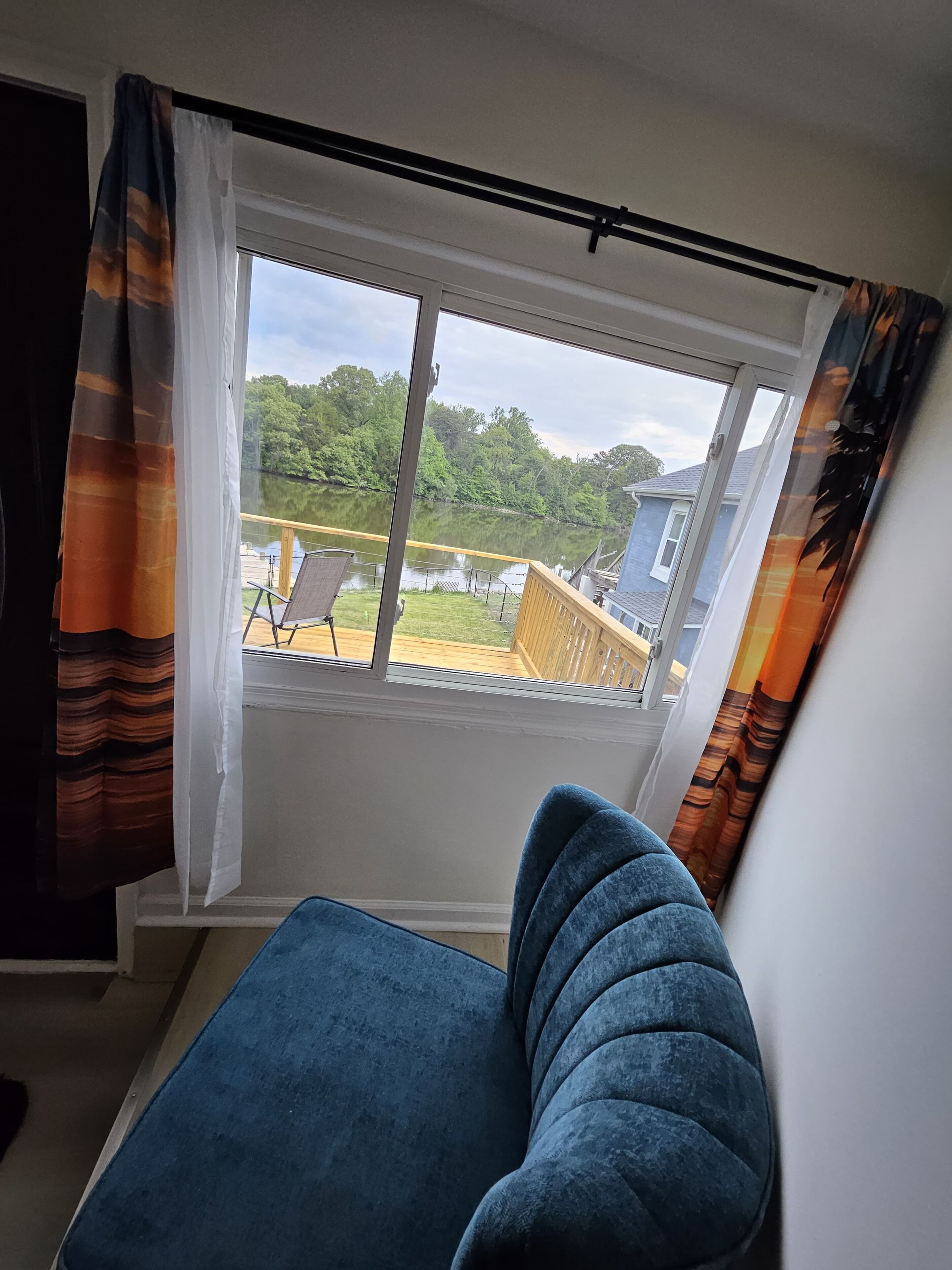 Ein Zimmer mit großem Fenster, blauem Sessel und Blick auf See und Bäume.
