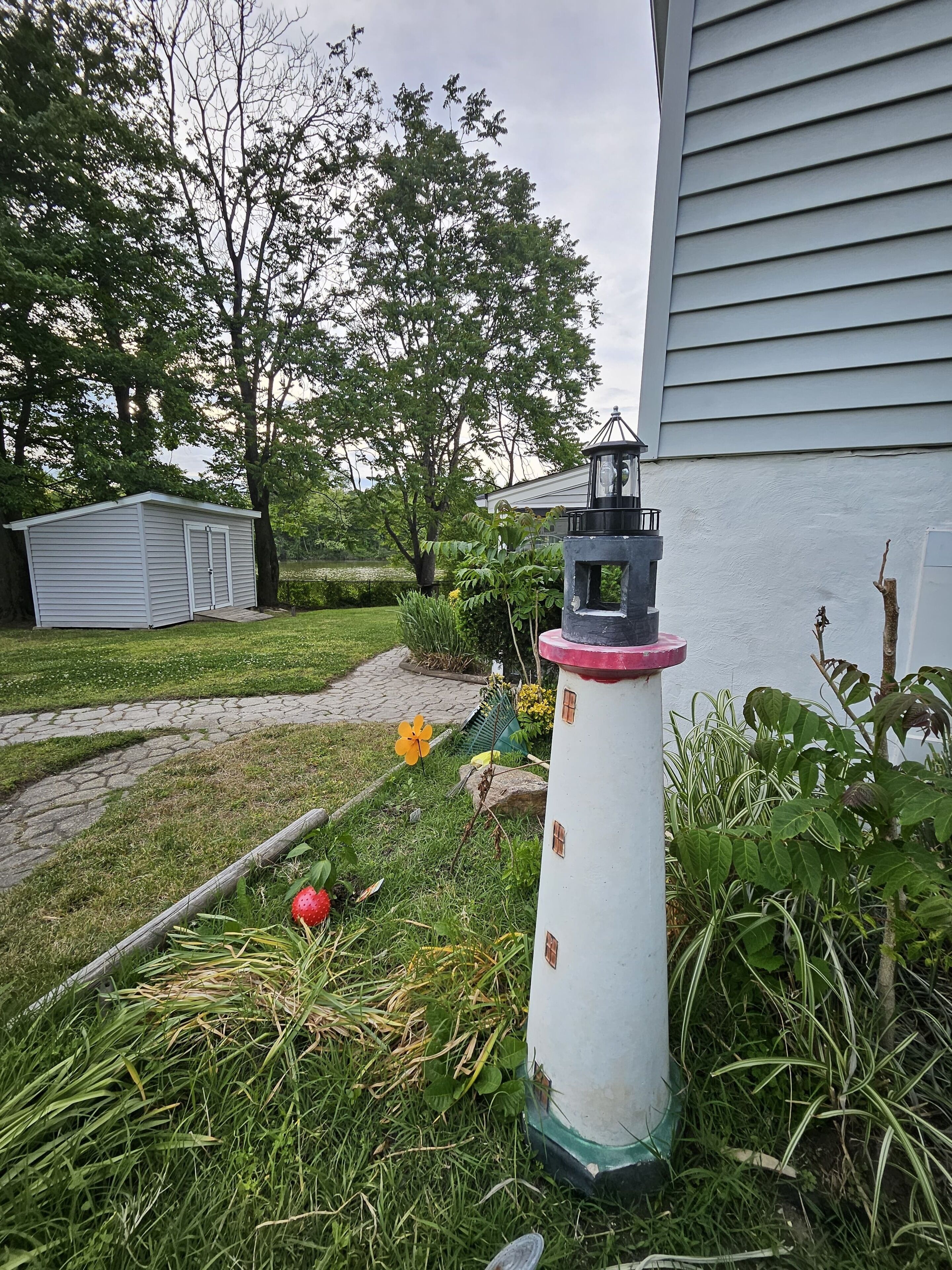 Ein weißer Leuchtturm mit roter Spitze, umgeben von viel Grün und einer kleinen Gartenhütte.