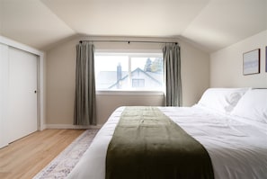 A bedroom with a bed, a window with curtains, a door, and a wall with framed pictures. - Modern Seattle Retreat (Seattle)