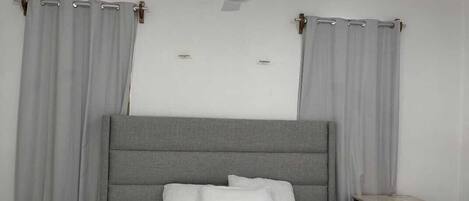 A bedroom with a bed, curtains, a ceiling fan, and a nightstand.