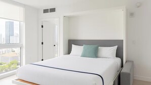 Et moderne hotelværelse med et stort vindue, en seng med hvide sengetøj, en grå sengegavl og et gråt natbord.