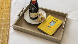 En bakke med en flaske Moët & Chandon champagne, en tallerken med chokolade og en bog med titlen 'Miami Cocktails'.
