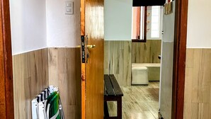 Ein Flur mit einer Holztür, einem Klappstuhl, einer Bank und einem Badezimmer im Hintergrund.