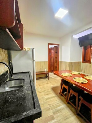 A kitchen with a black countertop, a wooden dining table with placemats, and a wooden door in the background. - House on Second Beach | 2 Bedrooms | 2 Bathrooms | Air Conditioning (Morro de São Paulo)