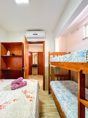 A room with a bunk bed, a wooden wardrobe, a desk, and an air conditioning unit.