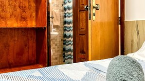 Ein Zimmer mit einem Bett, einem Holzschrank und einem durchgegangene Tür erkennbaren Badezimmer.
