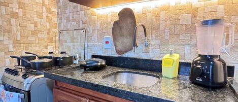 A kitchen with a granite countertop, a built-in oven, a sink, a blender, and a stove.