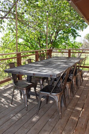 Eine Holzterrasse mit einem Metalltisch und Stühlen, umgeben von Bäumen.