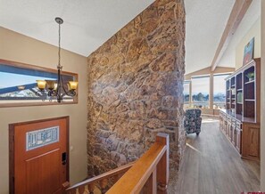 Ein geräumiger Innenraum mit Steinwand, Holztreppe und Ausblick durch ein Fenster.