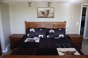 Une chambre à coucher avec un grand lit, une tête de lit ornée d’un motif à motifs de vaches et une taie d’oreiller aux mêmes motifs.