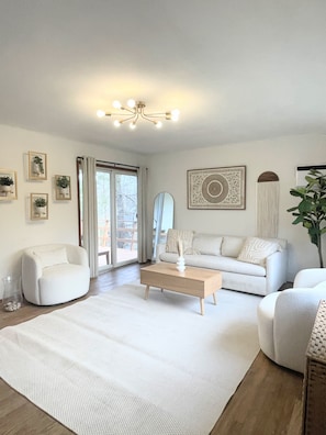 A modern living room with a white sofa, a coffee table, and a large window with curtains.