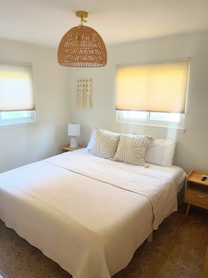 A bedroom with a large bed, two bedside tables, a hanging light fixture, and a macrame wall hanging.