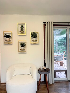 A room with a white armchair, a small round table with a bottle and glass, and four framed potted plants on the wall. - Charming 3-bedroom house in brilliant Sag Harbor Village with AC (Sag Harbor)
