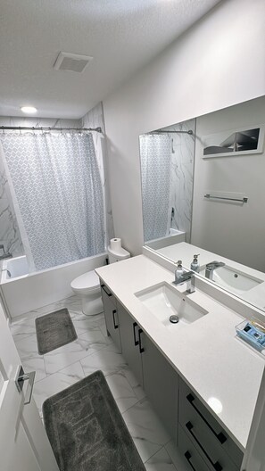 A modern bathroom with a bathtub, toilet, and sink. - HomeAwayFromHome- Free parking! (Fort Saskatchewan)