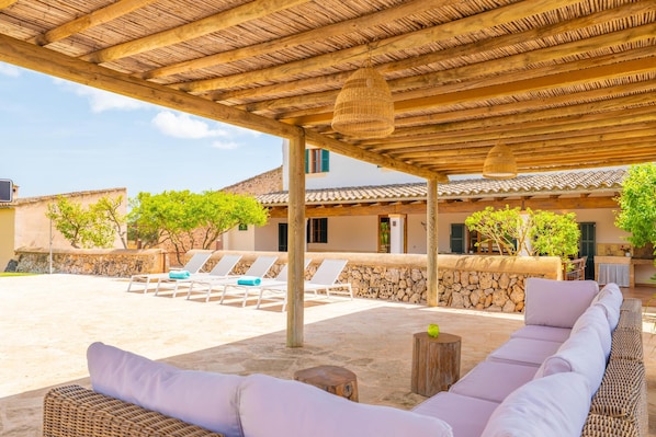 A covered outdoor seating area with lounge chairs and a wicker sofa.