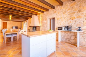 A spacious kitchen with a stone wall, wooden beams, a central island, and a dining area with chairs.