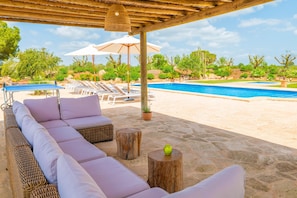 A poolside area with lounge chairs, a wicker sofa, and a pergola with umbrellas.