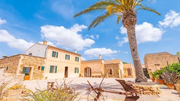 Un edificio in pietra tradizionale con cortile, palma e mobili da esterno rustici.
