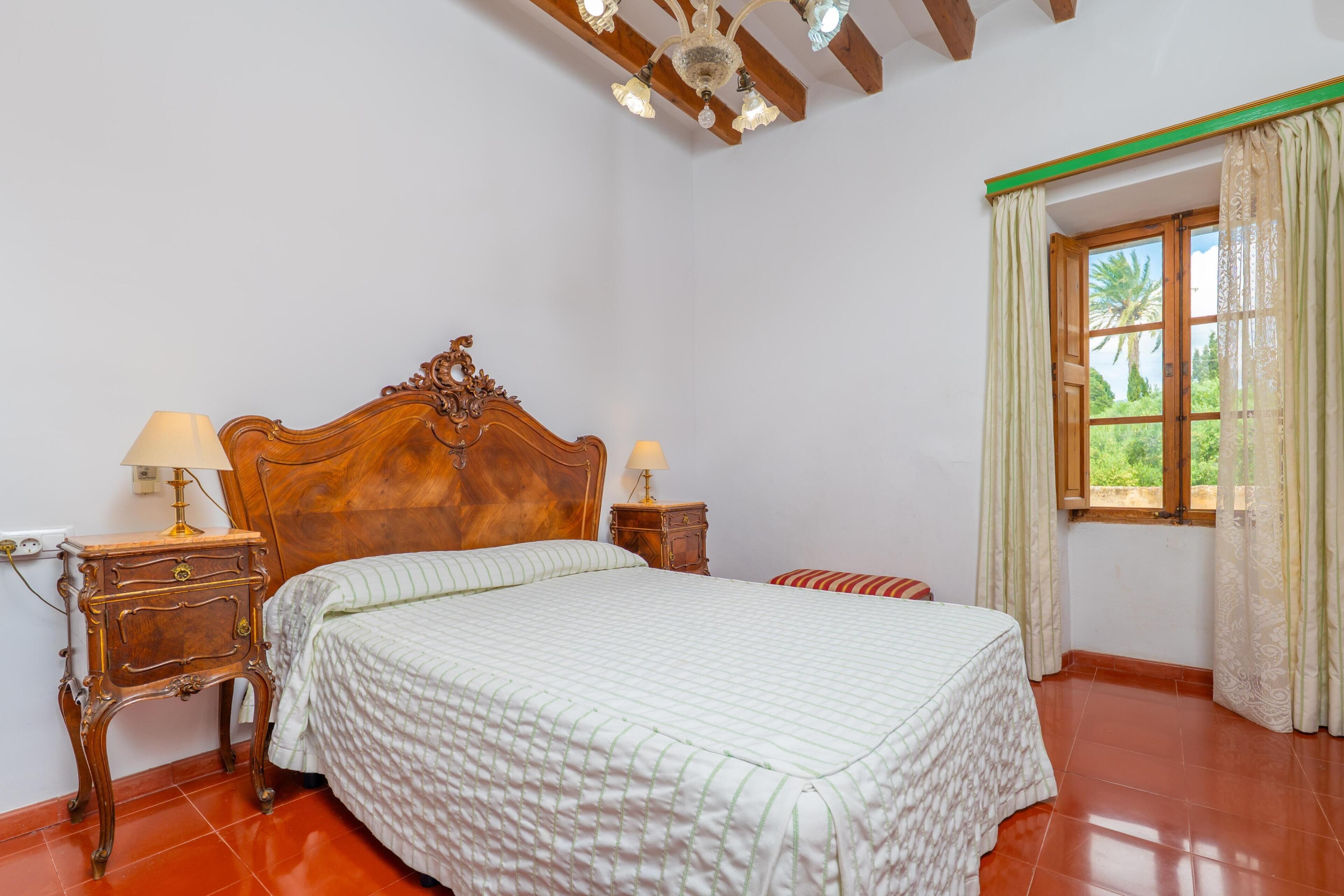 A bedroom with a wooden bed, two bedside tables, a window with curtains, and a tiled floor.