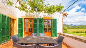 Eine Terrasse mit Tisch und Stühlen, grüne Fensterläden und Blick ins Grüne.