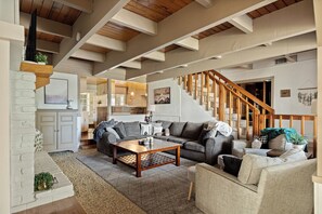 A spacious living area with a wooden staircase, a sofa set, and a coffee table. - Mountain Fun Lodge: Big Spaces, Big Views, Endless Games, Family Memories (Running Springs)