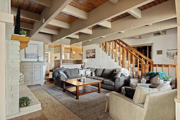 A spacious living area with a wooden staircase, a sofa set, and a coffee table. - Mountain Fun Lodge: Big Spaces, Big Views, Endless Games, Family Memories (Running Springs)