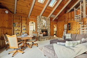 A wooden interior with a stone fireplace, a dining table with chairs, and a sofa. - Mountain Fun Lodge: Big Spaces, Big Views, Endless Games, Family Memories (Running Springs)