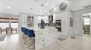 A modern kitchen with a marble island, bar stools, and stainless steel appliances.