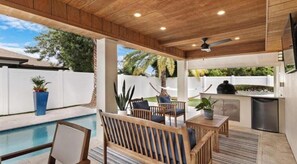 An outdoor patio with a pool, wooden furniture, and a barbecue area.