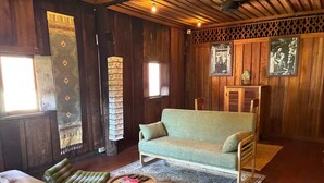 A wooden interior with a sofa, two green cushioned chairs, a round coffee table, and patterned rugs. - HoP:House of Peace in Heritage Area; walk to evthg (Luang Prabang)