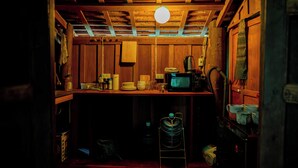 A dimly lit room with wooden walls and a ceiling, featuring a table with various items, a microwave, and a water dispenser. - HoP:House of Peace in Heritage Area; walk to evthg (Luang Prabang)
