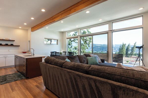 A modern living room with a sofa, dining table, and large windows offering a view of the outdoors. - Clearwater Summit: Panoramic Gorge Views & Modern Design (Hood River)