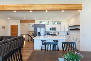 A modern kitchen with white cabinets, stainless steel appliances, and a central island with bar stools. - Clearwater Summit: Panoramic Gorge Views & Modern Design (Hood River)