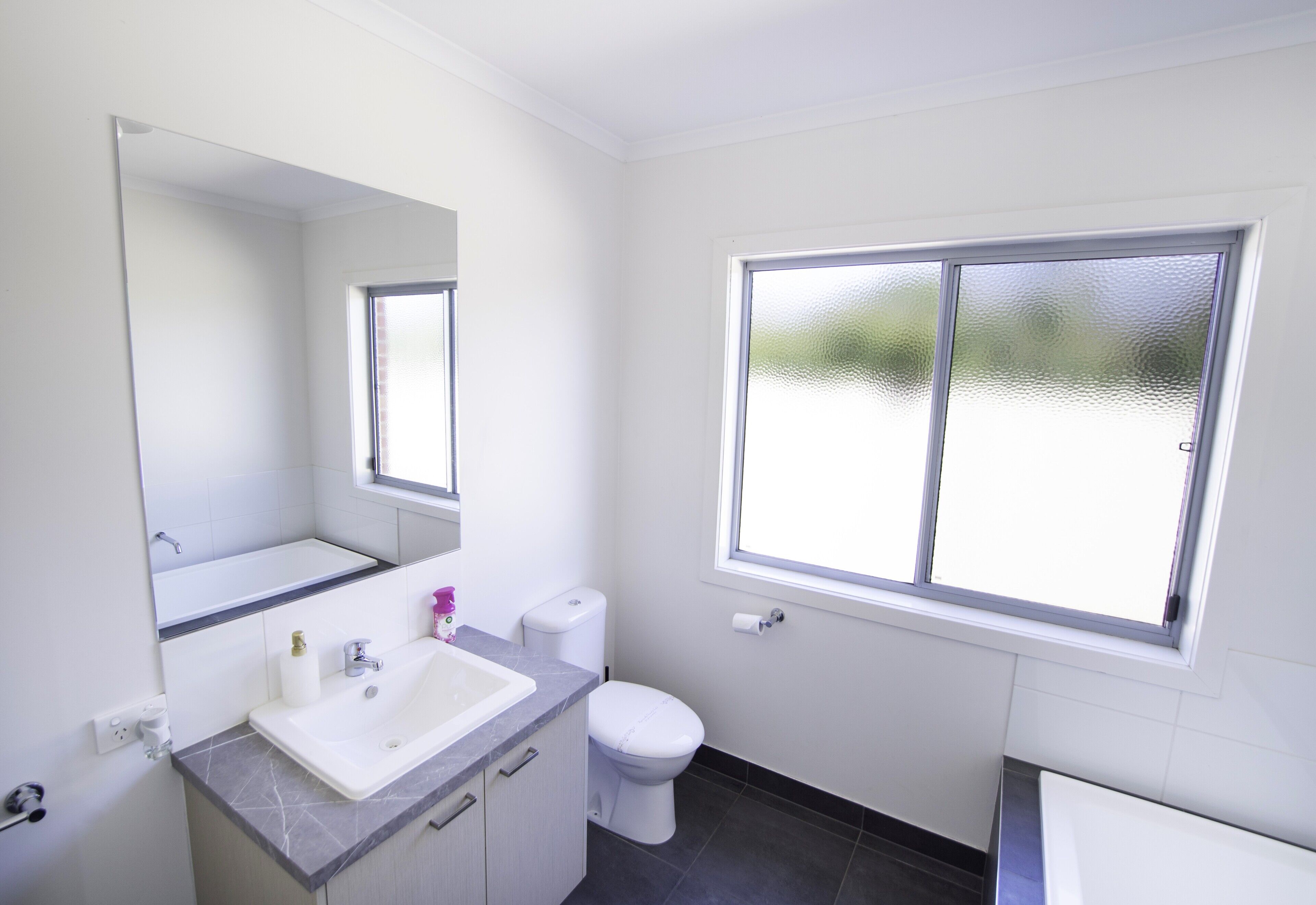 Ein Badezimmer mit Waschbecken, Spiegel, Toilette und Fenster.