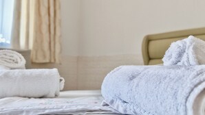 Een net opgemaakt bed met een witte spreidek en een opgerolde witte handdoek ernaast.