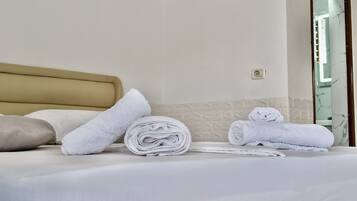 Una cama bien hecha con sábanas blancas, un cabecero color beige y una toalla enrollada al lado.