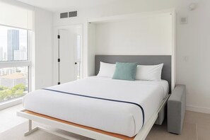 A modern hotel room with a large window, a bed with white bedding, a grey headboard, and a grey bedside table. - Luxury 2BR Downtown Miami Condo with City Views (Miami)