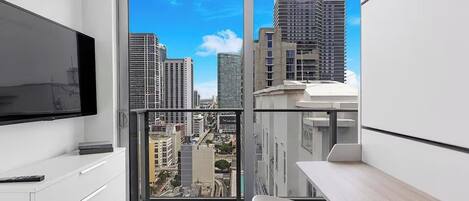 A modern apartment with a balcony, a TV, a dining area, and a city view.
