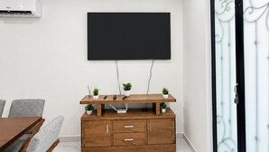 Ett modernt vardagsrum med en platt-TV som är monterad på väggen, en träinredd TV-möbel med växter, ett matbord med stolar och en skjutdörr i glas med dekorativa metallbeslag.