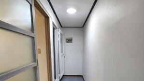 En smal gang med en dør til venstre, en lille indbygget loftslampe og et flisegulv.