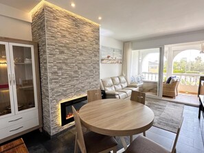 Ein modernes Wohnzimmer mit Kamin aus Stein, einem runden Holztisch und einer Sitzecke mit Sofa und Sesseln.