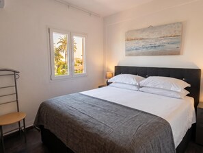 Ein Schlafzimmer mit Bett, Fenster mit Aussicht, Nachttisch mit Lampe und einem Gemälde an der Wand.